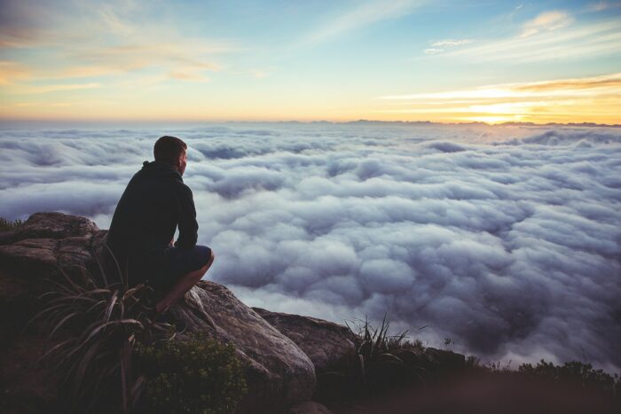 Man sitting on mountain with a view above the clouds.